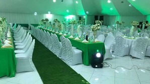 Un salón de banquetes con filas de mesas, alfombra verde y sillas blancas.