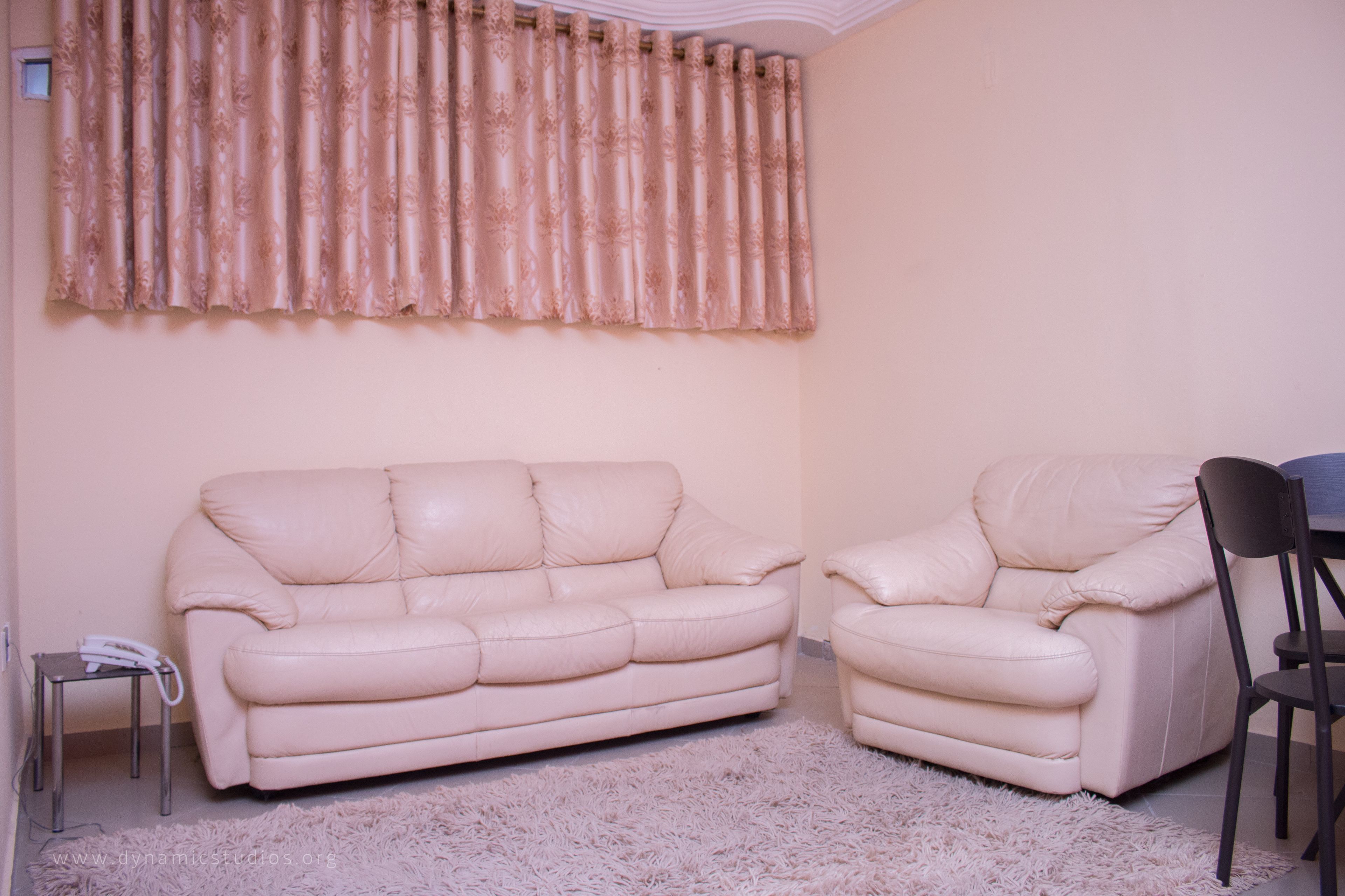 A living room with a beige sofa, a matching armchair, a small side table, and a fluffy rug.