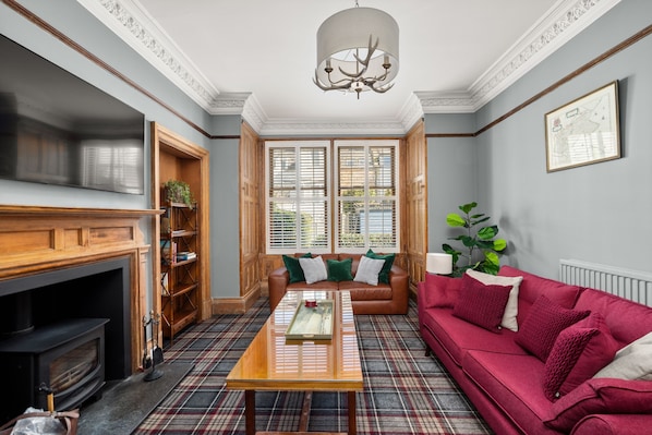 A living room with a fireplace, a plaid carpet, a red sofa, and a large window with blinds.