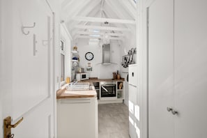 A narrow hallway leading to a kitchen with white walls, a wooden countertop, and a clock on the wall.