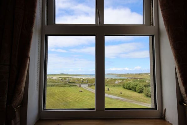 A window with a view of a rural landscape, including fields, a road, and distant hills. - Jackie´s Cottage, Claddaghduff (Claddaghduff)