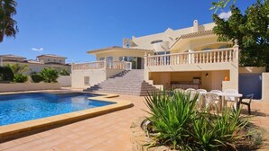 A pool area with a clear blue pool, a staircase leading to a balcony, and a seating area with white chairs. - Villa Cora - Javea, Costa Blanca (Javea)