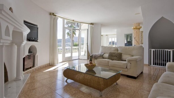 A spacious living room with a glass coffee table, a beige sofa, and a fireplace. - Villa Cora - Javea, Costa Blanca (Javea)