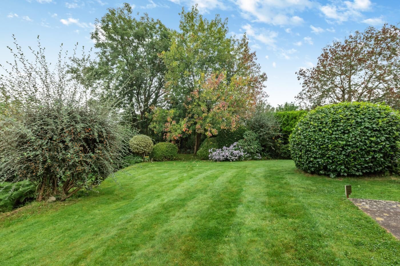 Un jardin bien entretenu, avec une variété d’arbres et d’arbustes, une pelouse soigneusement tondue et un ciel dégagé.