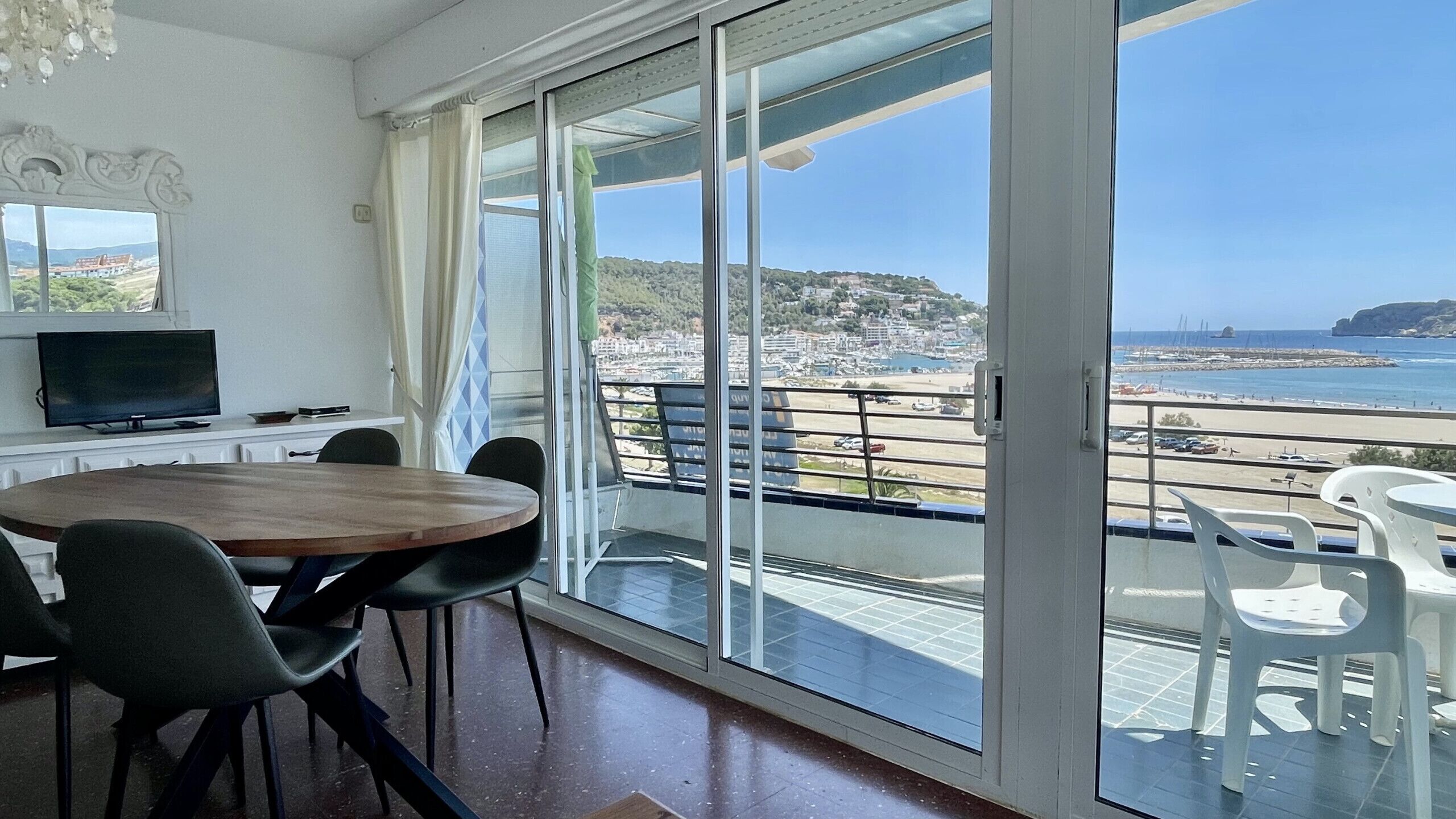 A room with a large sliding glass door leading to a balcony with a view of the beach and ocean.