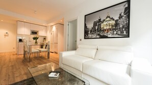 Una sala de estar moderna con un sofá blanco, una mesa de centro de vidrio y una zona de comedor con una mesa y sillas blancas.