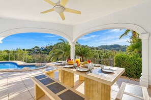 A covered outdoor dining area with a pool, a table set for breakfast, and a view of the landscape. - Villa Jarmila - Javea, Costa Blanca (Javea)