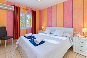 A hotel room with a bed, two bedside tables, a chair, an air conditioning unit, and a window with curtains. - Villa Jarmila - Javea, Costa Blanca (Javea)