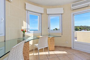 A corner room with a glass table, two chairs, a vase with flowers, and large windows with a view of the landscape. - Villa Jarmila - Javea, Costa Blanca (Javea)