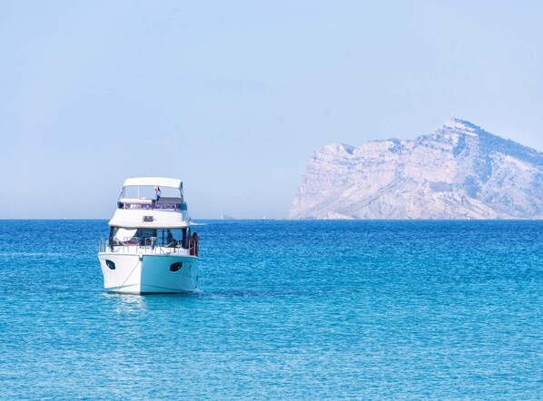 A white boat on calm blue waters with a rocky cliff in the background. - Villa Mila 10 - PlusHolidays (Calpe)
