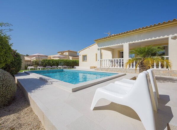 A swimming pool with lounge chairs, a covered patio, and a building with a tiled roof. - Villa Mila 10 - PlusHolidays (Calpe)