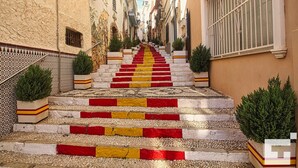 Un carrer estret amb una escala que puja a un edifici. Els graons tenen franges vermelles i grogues alternades.