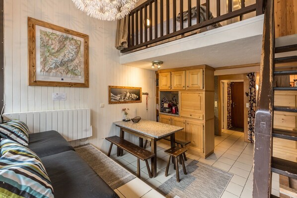 Ein gemütliches Zimmer mit einem Bett, einem Esstisch mit Bänken, einer Küchenzeile und einer Treppe zu einer oberen Ebene.