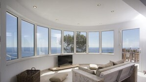 A modern living room with large windows, a flat-screen TV, and a built-in bench. - Modern and luxury holiday house in Javea, Costa Blanca, Spain  with private pool for 8 persons (Javea)
