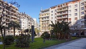 Um edifício residencial com várias varandas, um pátio central com uma fonte e vegetação ao redor.