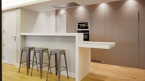 Cozinha moderna com bancada branca, banquetas de aço inoxidável e eletrodomésticos embutidos.