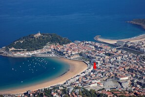 An aerial view of a coastal city with a prominent hilltop structure, a beach, and dense urban development.