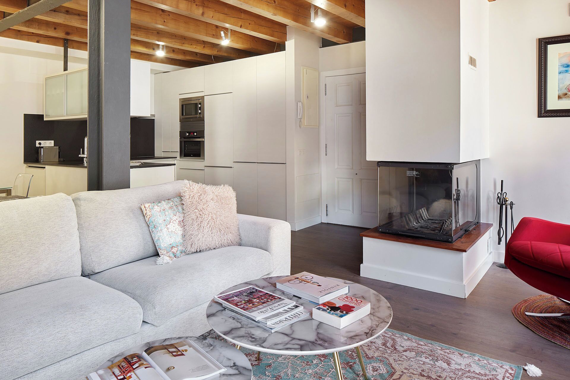 Una sala de estar moderna con un sofá, una mesa de centro con revistas, una chimenea y una cocina al fondo.