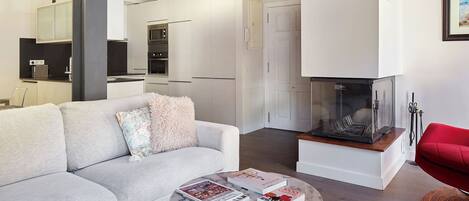 Una sala de estar moderna con un sofá, una mesa de centro con revistas, una chimenea y una cocina al fondo.