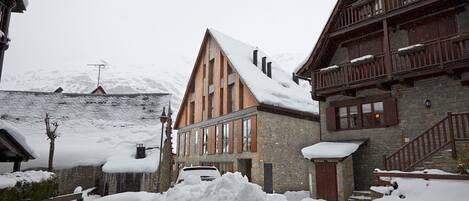 Ein schneebedecktes Gebäude mit einer Holzfassade und einem steinernen Sockel, mit einer Treppe und einem Balkon.