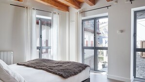 A bedroom with a bed, white curtains, and a view through a glass door to the outside. - Val Arties 3 by FeelFree Rentals (Arties)