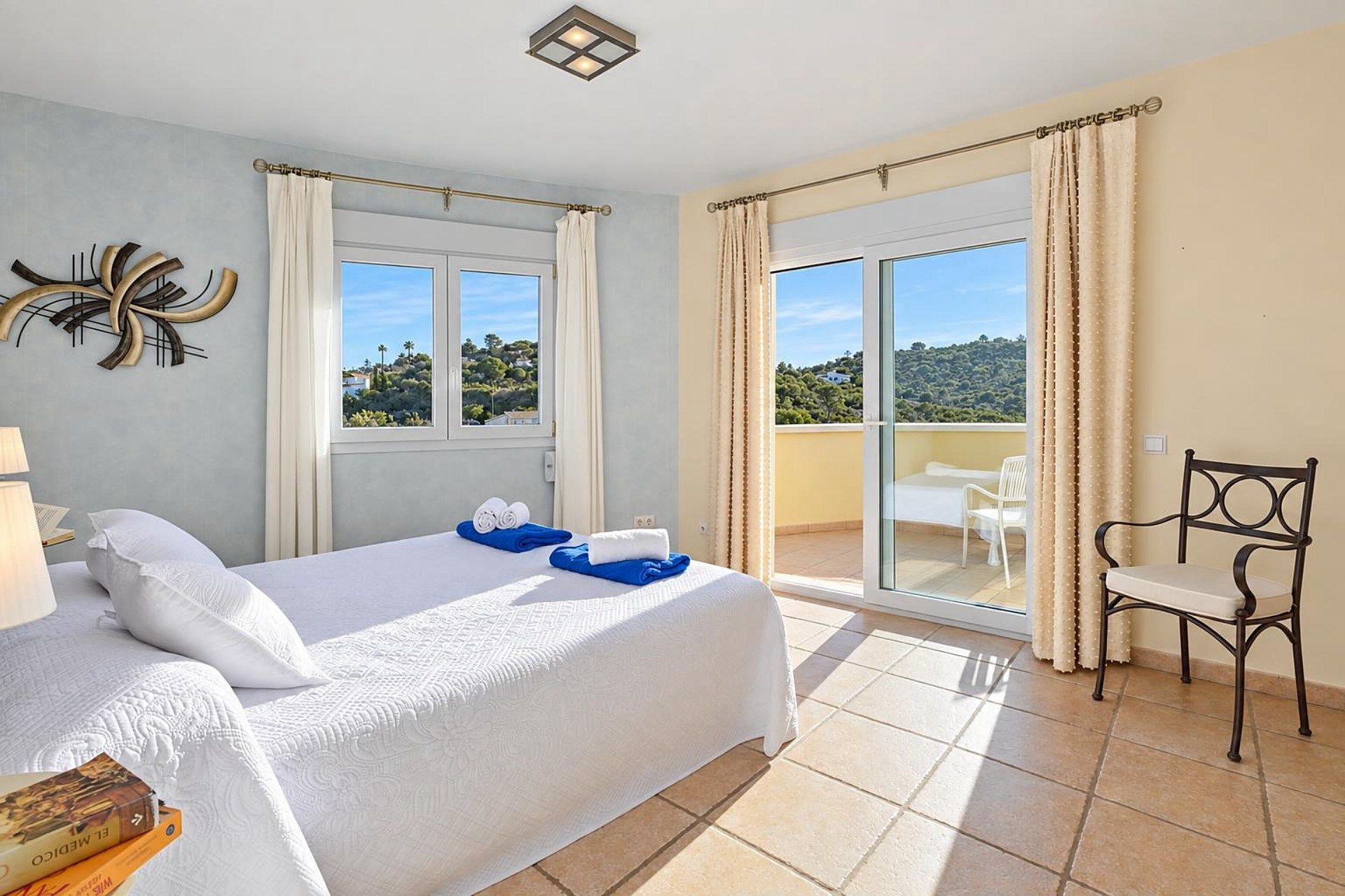 A hotel room with a bed, a chair, a table, and a view of the outdoors.