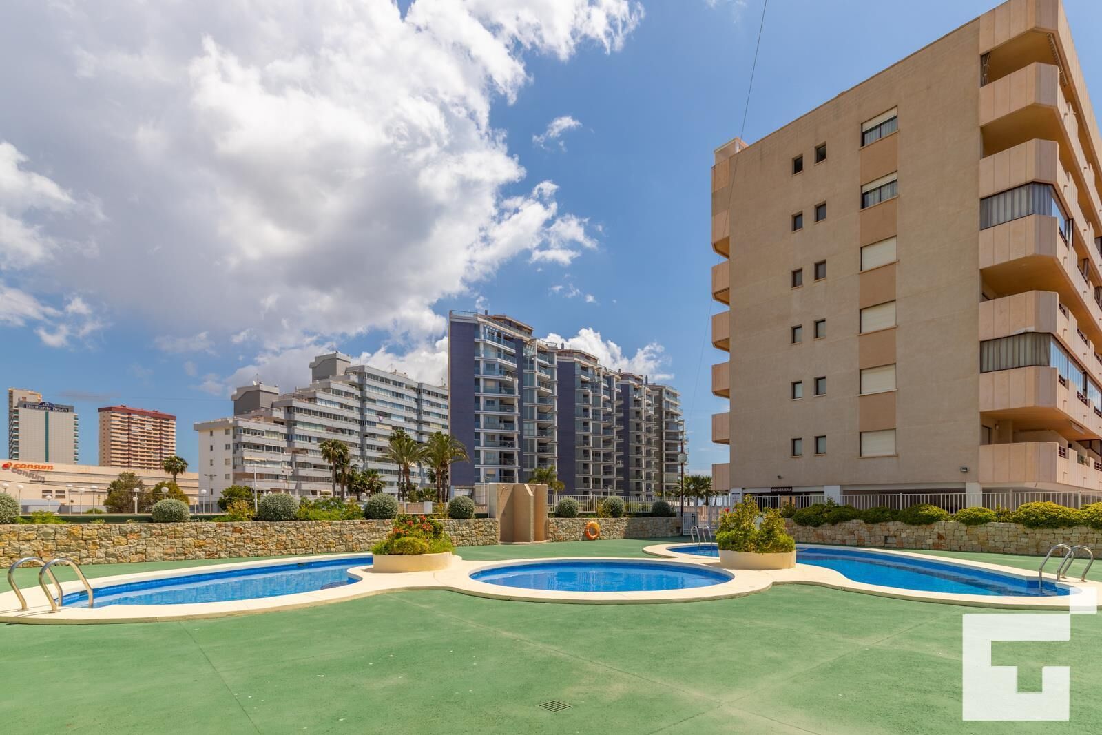 A modern apartment building with a pool area, including two swimming pools and a green lawn.
