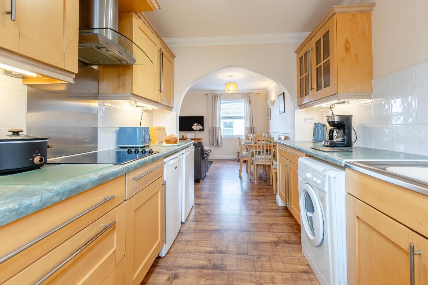 A kitchen with wooden cabinets, a stove, a washing machine, and a dining area with chairs and a table.