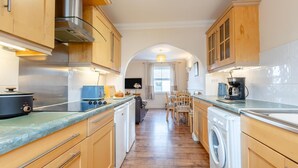 A kitchen with wooden cabinets, a stove, a washing machine, and a dining area with chairs and a table.
