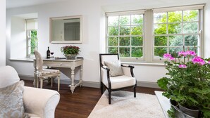 A room with a desk, two chairs, a large window with a view of greenery, and a potted plant with pink flowers. - A recently converted Kent ragstone coach house near Sevenoaks. (nr Sevenoaks)