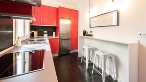 A modern kitchen with red cabinets, a stainless steel refrigerator, and a white countertop. - Chueca Urban (Madrid)