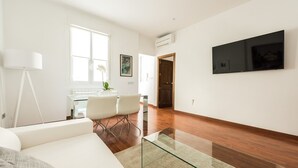 A modern living room with a glass coffee table, white sofas, and a dining area with a glass table and chairs. - Chueca Urban (Madrid)