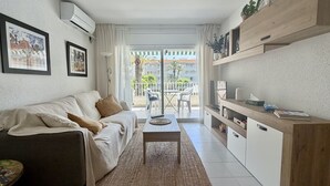 Un salon comprenant un canapé, une table basse, un téléviseur et un balcon offrant une vue sur les immeubles et les palmiers.