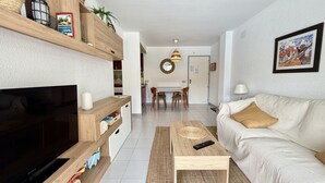 Un salon moderne doté d’un téléviseur à écran plat, d’étagères en bois, d’un canapé, d’une table basse et d’un coin repas avec des chaises et une table.