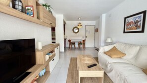 A living room with a TV, sofa, coffee table, and a dining area with chairs and a table.
