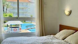 Une chambre d’hôtel avec un lit, une fenêtre donnant sur une piscine et un immeuble.