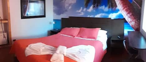 Habitación de hotel con cama, escritorio y un mural de palmera y cielo.