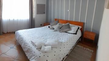 A bedroom with a bed, a nightstand, a hanging light fixture, and a window with curtains.
