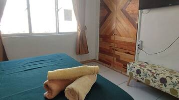 Una habitación con cama, televisor montado en la pared y ventana con cortinas.