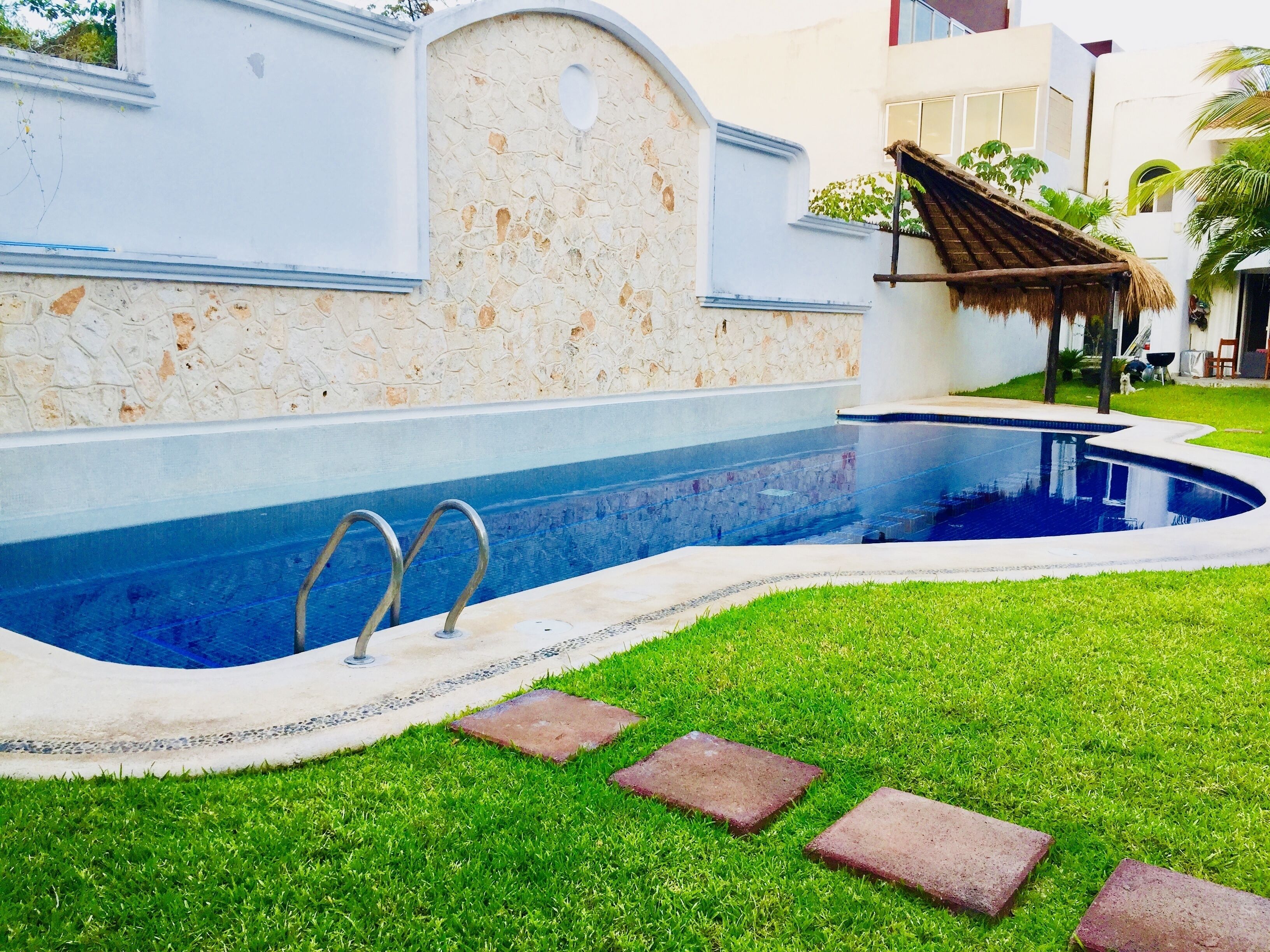 A swimming pool with a stone wall and a thatched roof structure.