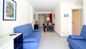 A living room with two blue sofas, a dining table with chairs, and a kitchen area in the background.