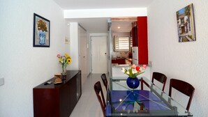 A dining area with a glass table and chairs, a vase with flowers, and a red door leading to a kitchen.