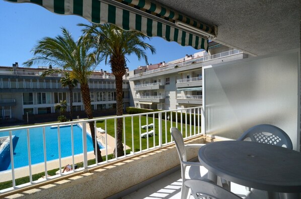 A balcony with a pool, palm trees, and a view of a multi-story building.