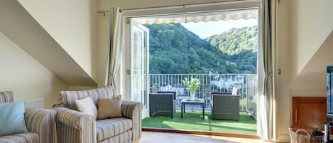 A living room with a sofa, a coffee table, and a balcony with a view of a mountain.