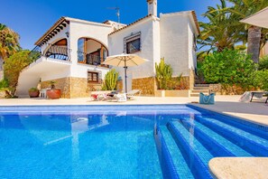 A poolside area with a clear blue pool, a two-story building with a balcony, and a stone facade. - Villa Quimera - PlusHolidays (Benissa)