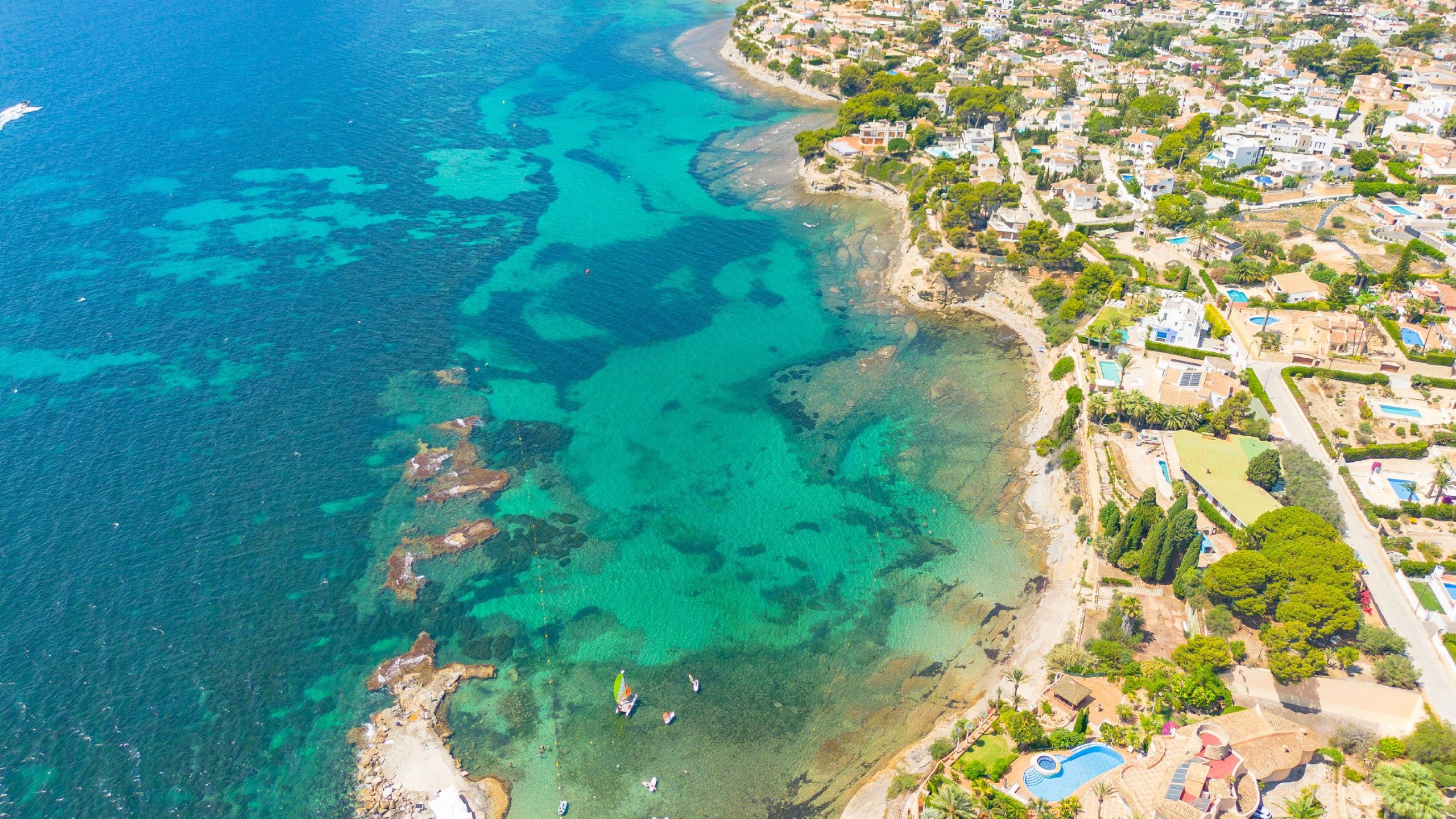 An aerial view of a coastal town with clear turquoise waters, a sandy beach, and residential buildings.
