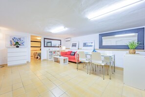 A modern living room with a red sofa, white chairs, and a dining area with a white table and chairs. - Villa Quimera - PlusHolidays (Benissa)