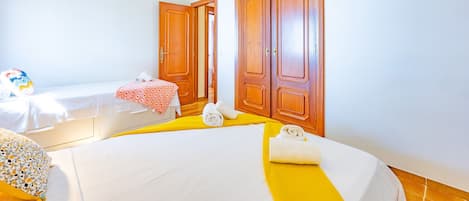 Quarto de hotel com duas camas, um candelabro, ar condicionado, guarda-roupas de madeira e uma pequena mesa com toalha xadrez vermelha e branca.