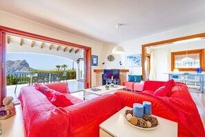 A bright living room with red sofas, a TV, and a dining area with a table and chairs. - Villa Quimera - PlusHolidays (Benissa)