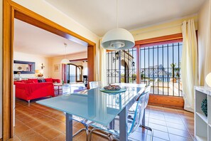 A spacious living area with a glass dining table, red sofa, and a balcony with a view of the mountains. - Villa Quimera - PlusHolidays (Benissa)